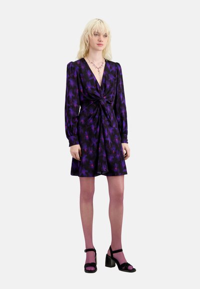 Vestido de flores morado con un escote en V profundo, detalle de frente torcido, mangas largas y una falda acampanada. Combinado con sandalias negras de tacón.