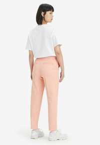 Vit cropped t-shirt i kombination med ljusrosa raka byxor. Byxorna har bakfickor och en diskret varumärkesetikett nära midjan.