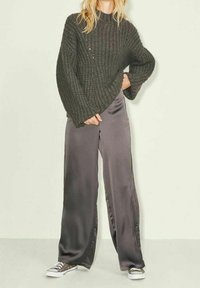 Chunky dark green knitted sweater with wide sleeves, paired with gray satin wide-leg pants and gray sneakers.