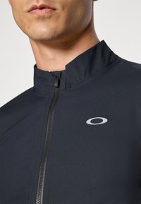 Black zip-up jacket made of textured fabric with a high collar, featuring a small silver logo on the left side.