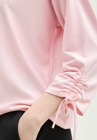 Helles pinkes Langarmshirt mit schmalen weißen Streifen. Verfügt über geraffte Bündchen mit Bändern und eine lockere Passform. Weicher, strukturierten Stoff.