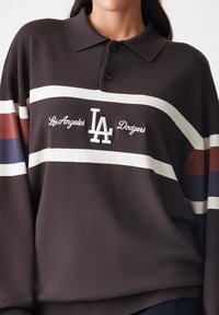 Bruine poloshirt met drie horizontale strepen in het wit, rood en marineblauw. Geborduurd "LA Dodgers" en logo op de voorkant.