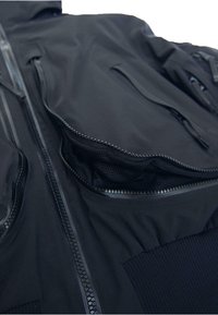 Fekete dzseki több cipzáras zsebbel, sima anyagból, texturált béléssel és elasztikus részletekkel. Testhezálló szabással és tartós cipzárakkal.