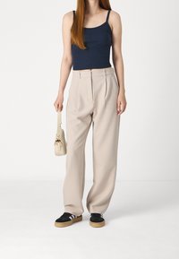 Marineblauw cropped tanktop, beige wijde broek met plooien, zwarte sportschoenen met witte strepen, en een kleine crème kleurige handtas.
