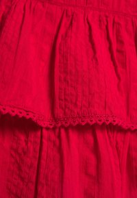 Tissu rouge avec des plis verticaux texturés et une bordure en dentelle festonnée le long du bord, en gros plan.