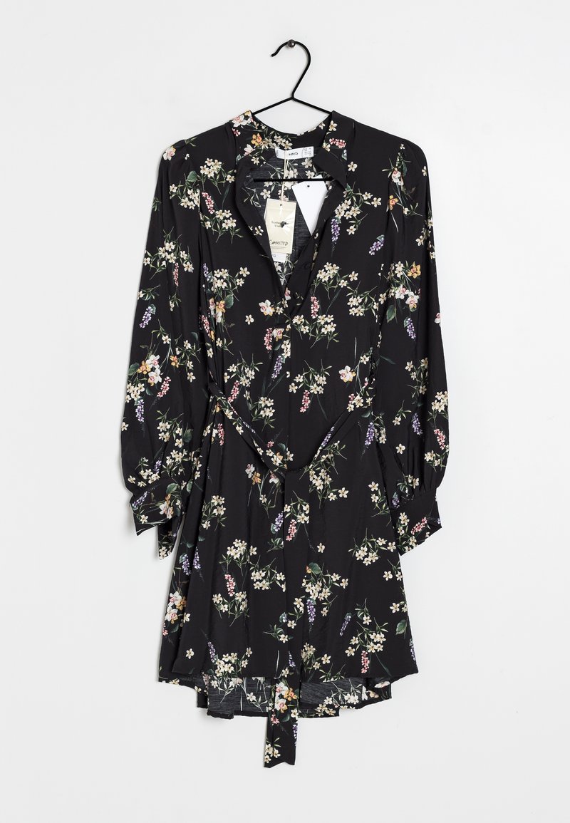 Robe noire à manches longues à fleurs avec de petites fleurs blanches, roses et violettes, suspendue sur un cintre noir avec des étiquettes attachées.