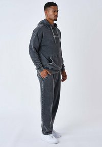 Conjunto de sudadera con capucha gris y pantalones de chándal en un aspecto descolorido y desgastado. Presenta un bolsillo tipo canguro, capucha ajustable con cordón y tejido texturizado a juego. Zapatillas blancas.