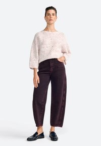 Maglione fuzzy rosa chiaro con scollatura ampia, abbinato a jeans a gamba larga viola scuro a vita alta. Mocassini neri completano l'outfit.