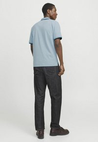 Ljusblå polo med marinblå detaljer, tillsammans med mörka denimbyxor och bruna skor. Skjortan har en klassisk krage och korta ärmar.