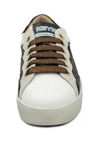 Sneaker bianco con lati in tessuto marrone texturizzato, punta rotonda, lacci marroni, occhielli dorati e suola grigia chiara che mostra una texture screpolata.