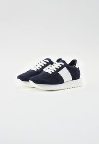 Baskets en suede bleu marine avec des accents blancs. Design classique à lacets, surface texturée et semelle en caoutchouc blanc épais avec un motif en zigzag.