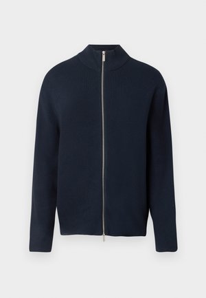 Jūrinės geltonos spalvos zip-up megztinis su aukšta apykakle, ilgomis rankovėmis ir lygiu paviršiumi. Yra sidabrinis užtrauktukas ir minimalistinis dizainas.