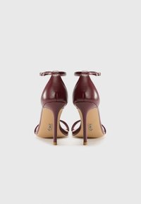 Escarpins en cuir bordeaux avec un design à lanières, boucle à la cheville et talon aiguille. Fini texturé, détail de logo subtil sur la semelle.