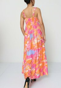 Robe maxi présentant un motif tie-dye coloré dans des tons de rose, orange et bleu clair. Elle a des bretelles fines et un design de jupe à volants.