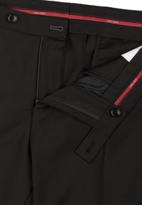 Schwarze Hose mit glatter Textur, ausgestattet mit einem Knopfverschluss, Reißverschluss und einem taillierten Etikett mit roten Akzenten. Innen gibt es eine Tasche.