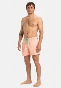 Breskevasto roza kopalne kratke hlače s turkizno vrvico, elastičnim pasom in lahkim materialom. Brez vidnih vzorcev ali grafik.