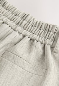 Light gray, woven fabric with a herringbone pattern. Features an elastic waistband and a single back pocket. Soft texture.