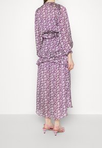 Robe longue violette à fleurs avec taille froncée et ourlet à volants. Tissu transparent, manches longues, assortie à des sandales à talons roses pâles.