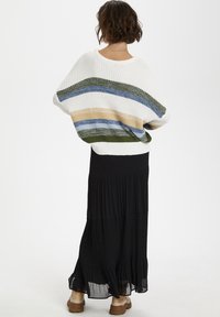 Suéter de punto holgado en crema con rayas verdes, azules y beige; combinado con una falda negra con volantes y zapatos de plataforma color beige.