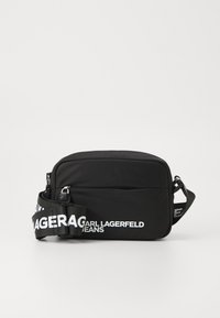 Schwarze Umhängetasche mit glatter Textur. Verfügt über ein Reißverschlussfach und einen Tragegurt mit weißer Schrift, auf dem "CARL LAGERFELD JEANS" steht.