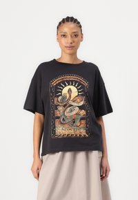 Svart oversized T-skjorte med et fargerikt grafisk design av slanger og sol. Mykt bomullsstoff med avslappet passform og kortermede ermer.