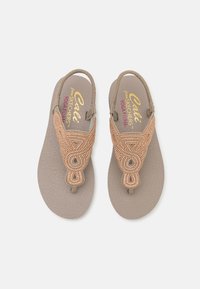 Beige flip-flopit, joissa on teksturoitu pohja ja koristeellinen helmistrap, joka esittelee monimutkaisen suunnittelun ja varvaspanta tukemaan jalkaa.