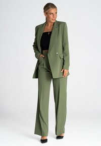 Oliwkowa marynarka i dopasowane spodnie w stylu taliowanym, podwójnie zapinane i z akcentami srebrnych guzików. Czarny top crop pod spodem.