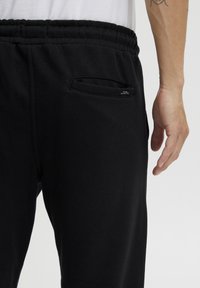 Pantalones jogger de algodón negros con cintura elástica, que cuentan con un bolsillo lateral. La tela tiene una textura suave y un ajuste casual.