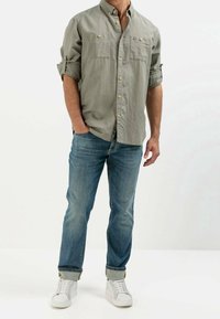 Lichtgrijs overhemd met knopen en opgerolde mouwen, twee borstzakken, gecombineerd met blauwe spijkerbroek en witte sneakers.