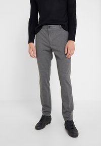 Grijze geweven broek met een getailleerde pasvorm, met een gladde textuur en een knoopsluiting. Gecombineerd met zwarte sportieve schoenen.