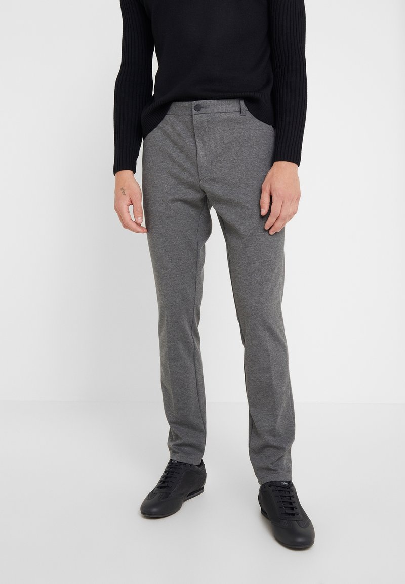 Grijze geweven broek met een getailleerde pasvorm, met een gladde textuur en een knoopsluiting. Gecombineerd met zwarte sportieve schoenen.