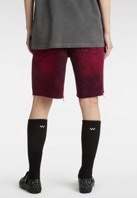 Pantalones cortos de mezclilla roja con un aspecto desgastado y dobladillo deshilachado, combinados con calcetas negras hasta la rodilla que presentan detalles en blanco a cuadros.