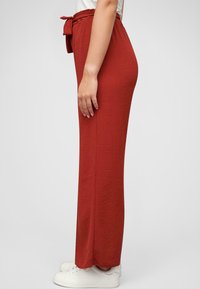 Pantaloni rossi larghi realizzati in un tessuto morbido, con una vita legata e un design a gamba dritta. Indossati con scarpe da ginnastica bianche.
