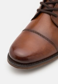 Gros plan sur une chaussure habillée en cuir marron avec des lacets brun foncé et des coutures détaillées sur le bout et la semelle.