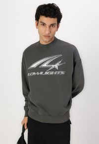 Dark gray sweatshirt with ribbed cuff, crew neckline, and a large graphic print featuring a stylized number and star on the front.
