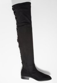Botte noire au-dessus du genou en tissu doux, avec un talon plat, une texture lisse et des détails décoratifs à lacets sur le côté.