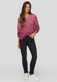 Rosa und lila gestreifter Strickpullover mit rundem Ausschnitt, kombiniert mit schwarzen, schmal zulaufenden Jeans und weißen Sneakern. Glatte Textur, lockere Passform.