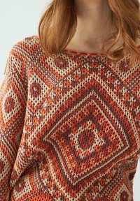 Sweter dzianinowy z geometrycznym wzorem w odcieniach pomarańczowym, kremowym i brązowym; szeroki dekolt; teksturowany materiał o przytulnym wyglądzie.