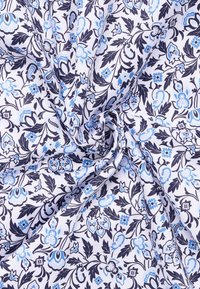 Witte stof met een bloemengrafiek met blauwe en marine bloemen, bladeren en paisley ontwerpen, met zichtbare textuur en draping.