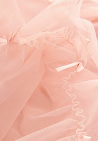 Tessuto di tulle rosa con bordi arricciati e piccoli dettagli a forma di fiocco. La texture è morbida e leggera, con materiale trasparente a strati.