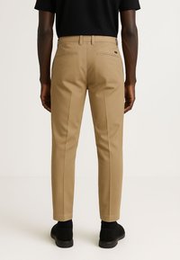 Pantaloni khaki con vestibilità sartoriale, dotati di due tasche posteriori e tessuto liscio, abbinati a calzature nere.