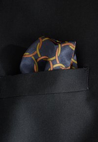 Silk pocket square with a pattern of interlinked circles in orange and yellow on a dark blue background, placed in a black suit pocket.