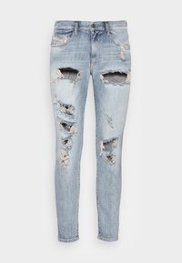Vaqueros de denim azul claro con múltiples áreas desgastadas y grandes roturas. Presentan un diseño clásico de cinco bolsillos y cierre de botón.