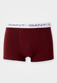 Boxer briefs de algodón burdeos con una cinturilla elástica blanca que presenta el nombre de la marca "GANT" en azul marino. Las costuras son visibles a lo largo de los bordes.