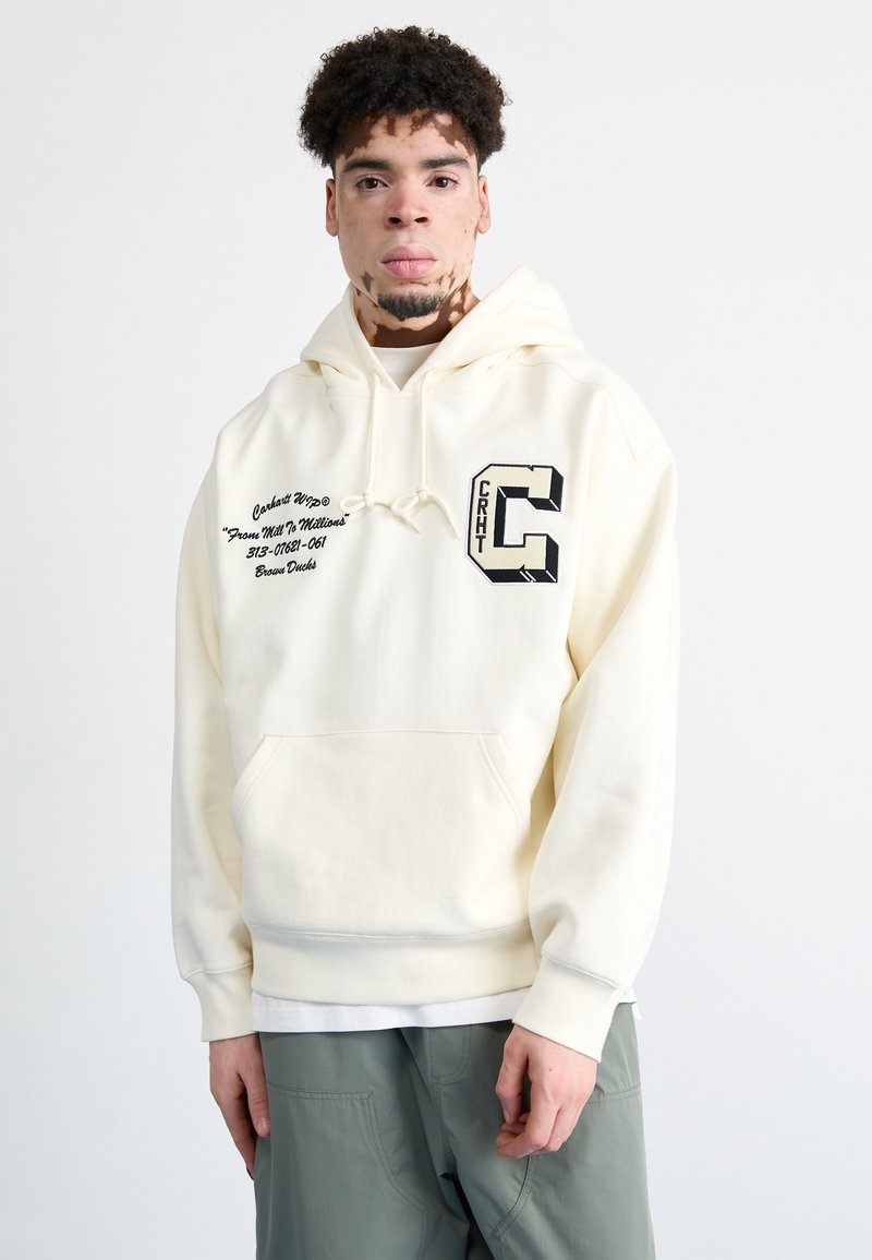 Sudadera de color crema con un bolsillo frontal tipo pouch, capucha con cordón y detalles gráficos en negro que incluyen texto y una letra "C" en el pecho.