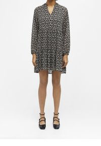 Robe noire à fleurs avec des manches longues, un décolleté en V et un ourlet en tiers. Fabriquée en tissu léger, elle arbore de petits motifs floraux blancs.