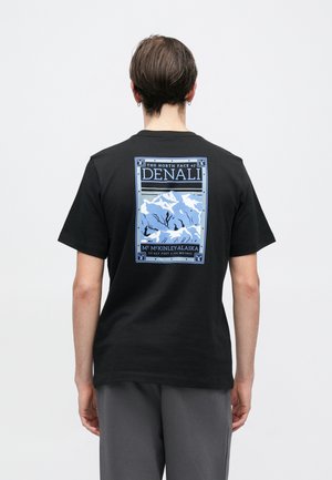 Melnas kokvilnas T-krekls ar zilas grafikas dizainu uz muguras, kurā attēlotas kalnu virsotnes ar tekstu: "The North Face of Denali, Mt. McKinley, Alaska."