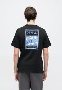 Μαύρο βαμβακερό μπλουζάκι με μπλε γραφικό σχέδιο στην πλάτη, που απεικονίζει βουνά με το κείμενο: "Η βόρεια πλευρά του Denali, Mt. McKinley, Αλάσκα."