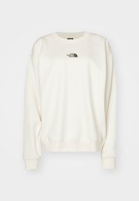 Sweatshirt crème clair avec un col rond, des poignets et un ourlet côtelés, présente un petit logo sur la poitrine en gris foncé. Texture douce.