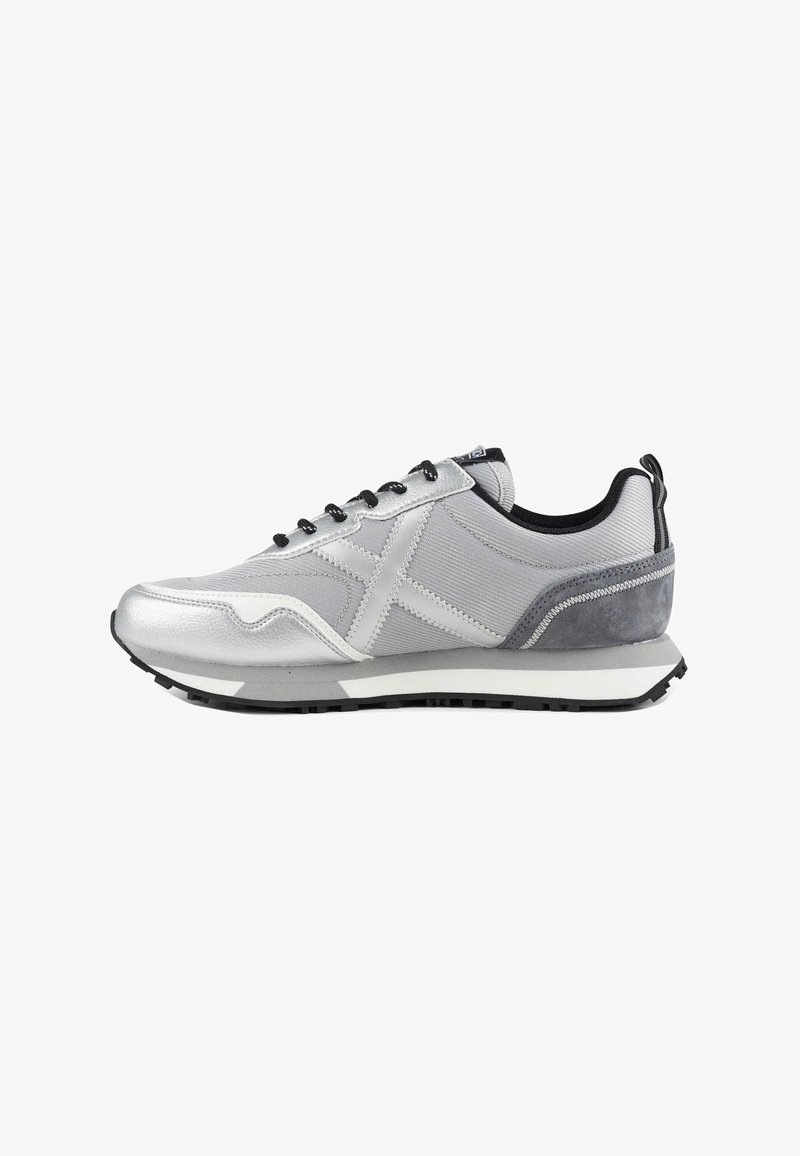 Baskets de sport grises et argentées avec lacets noirs, semelle blanche et semelle extérieure noire en vue de profil sur fond blanc.